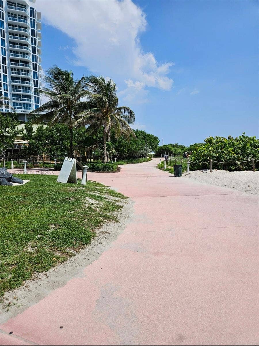 6365 Collins Avenue, #909, Miami Beach, FL 33141 Paved walkway featuring coastal landscaping, mature palm trees, manicured turf, and sandy beach border