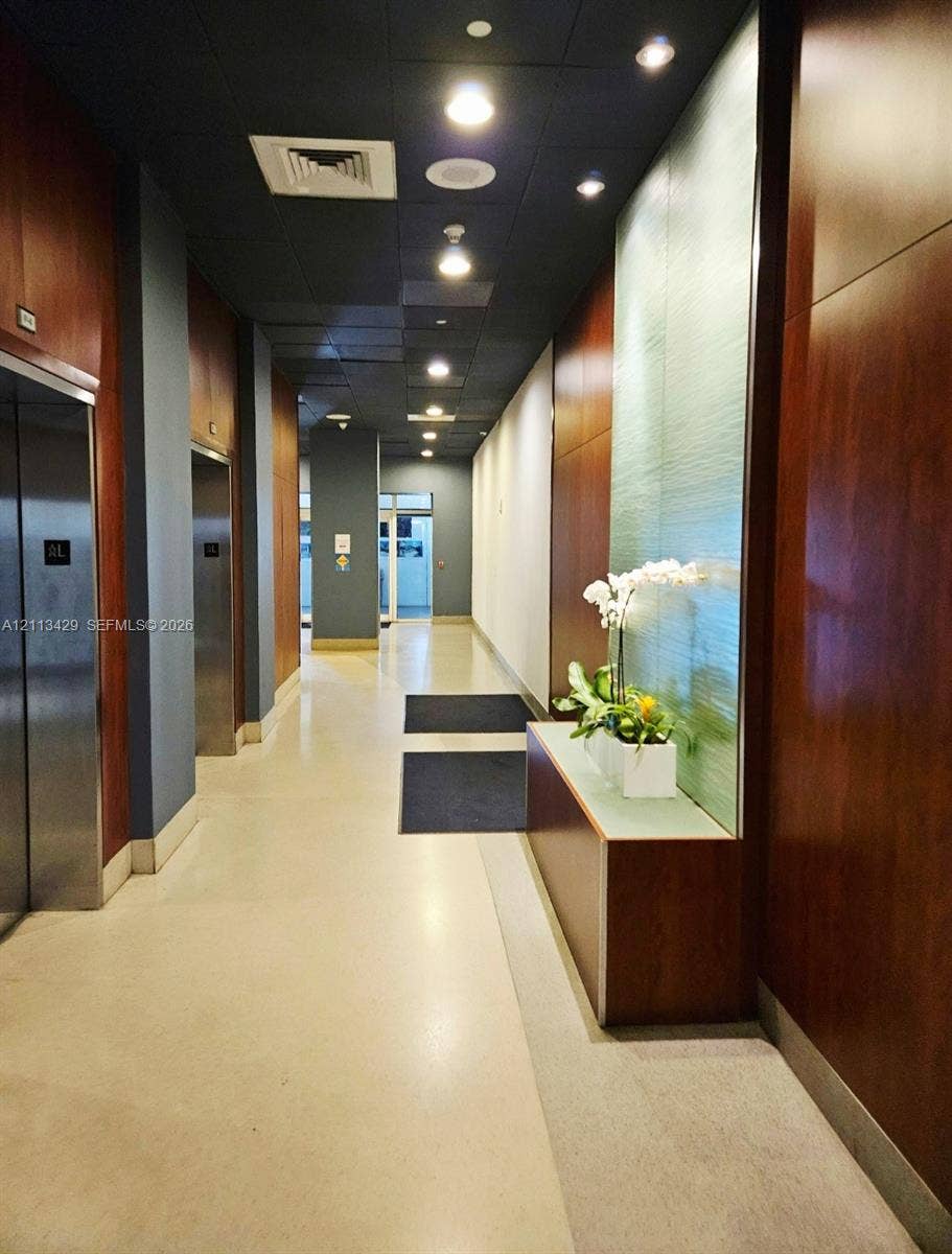 6365 Collins Avenue, #909, Miami Beach, FL 33141 Hallway featuring polished concrete flooring, full-height wood-finish wall paneling, recessed ceiling lighting, and a built-in illuminated decorative accent wall