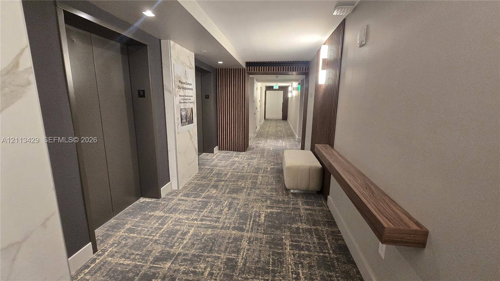 6365 Collins Avenue, #909, Miami Beach, FL 33141 Elevator lobby featuring metallic elevator doors, stone-finish wall accents, vertical wood slat paneling, wall-mounted linear lighting, and a fixed wood-finish floating console