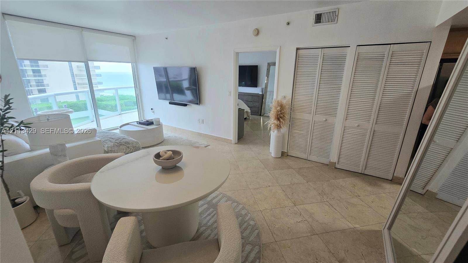 6365 Collins Avenue, #909, Miami Beach, FL 33141 Living area featuring floor-to-ceiling windows, natural stone tile flooring, dual sets of louvered-panel closet doors, and a glass-railed balcony