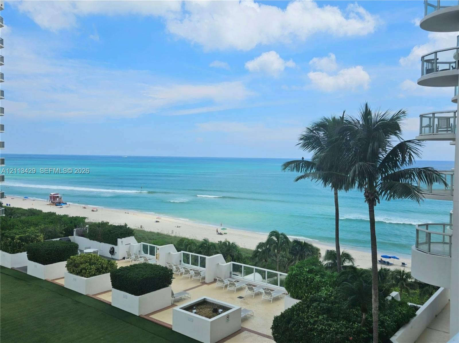 6365 Collins Avenue, #909, Miami Beach, FL 33141 Elevated terrace featuring a stone-tile floor, built-in concrete planters with mature greenery, and metal-railing balconies overlooking the ocean and sandy coastline