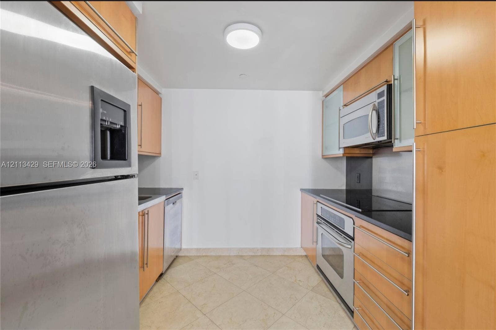 6365 Collins Avenue, #909, Miami Beach, FL 33141 Galley kitchen featuring light wood cabinetry, stone countertops, stainless steel appliances, and tile flooring