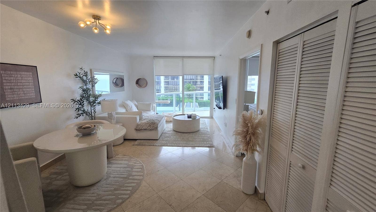 6365 Collins Avenue, #909, Miami Beach, FL 33141 Living area featuring large-format tile flooring, louvered-style closet doors, glass sliding doors, and a multi-bulb flush-mount light fixture