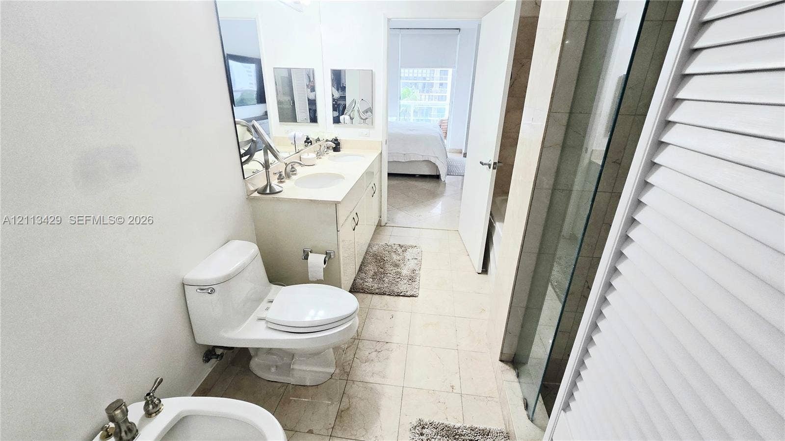 6365 Collins Avenue, #909, Miami Beach, FL 33141 Bathroom featuring a dual-sink vanity with light-toned cabinetry, stone countertop, wall-to-wall mirror, glass-enclosed shower, and tile flooring