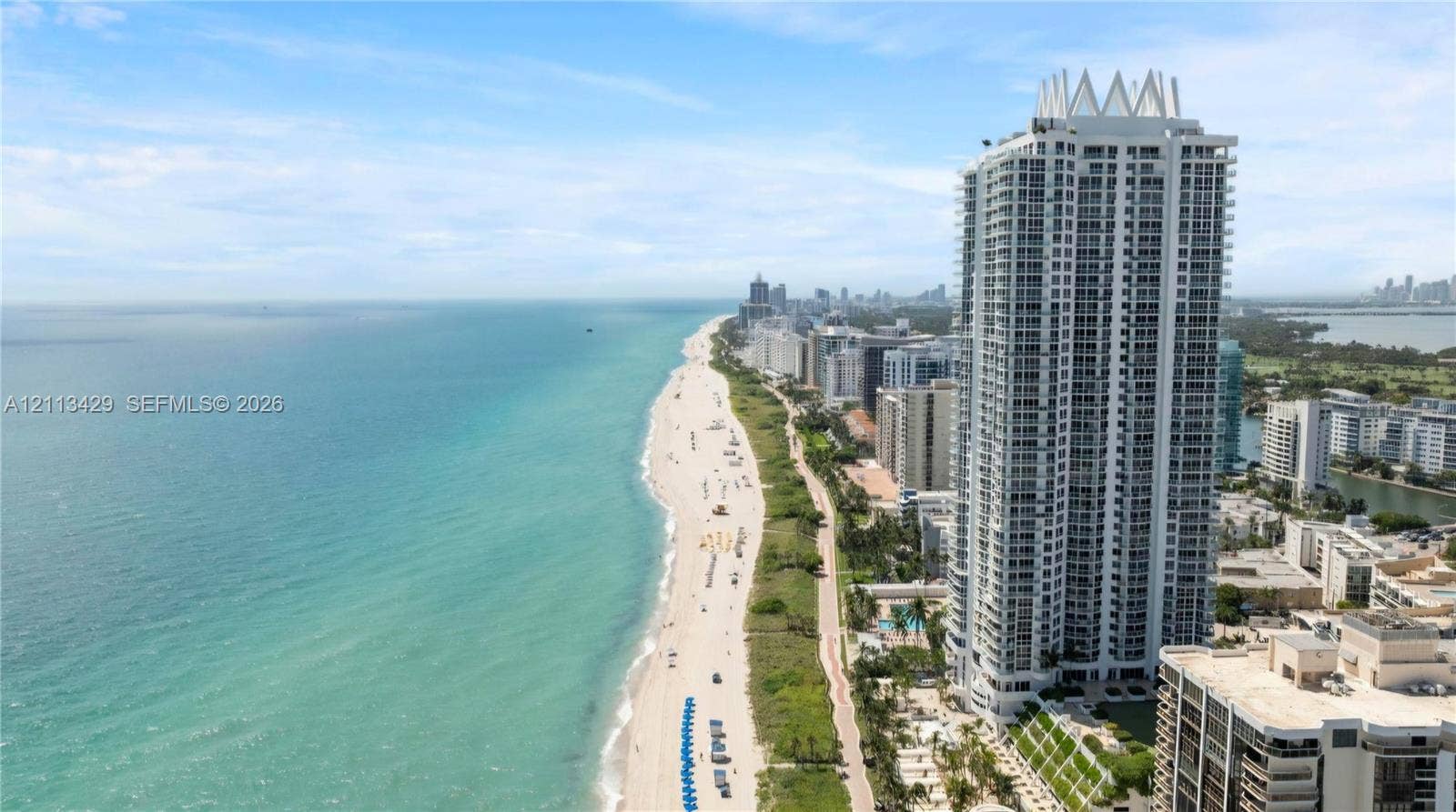6365 Collins Avenue, #909, Miami Beach, FL 33141 High-rise residential tower featuring a multi-story exterior, glass balconies, tiered architectural crown, and direct shoreline proximity