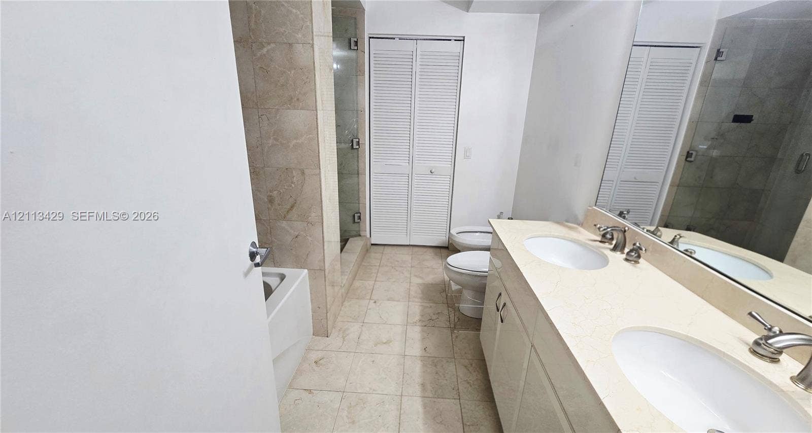 6365 Collins Avenue, #909, Miami Beach, FL 33141 Bathroom featuring a dual-sink vanity with a stone countertop, a glass-enclosed shower, a soaking tub, and louvered bifold closet doors