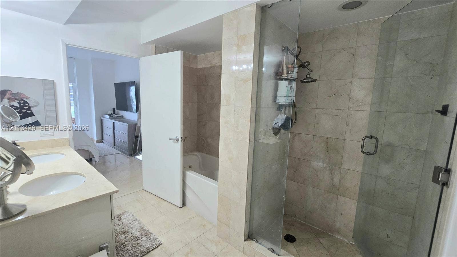 6365 Collins Avenue, #909, Miami Beach, FL 33141 Dual-sink vanity with light-toned countertop, soaking tub, glass-enclosed shower with stone-tile surround, and tiled flooring