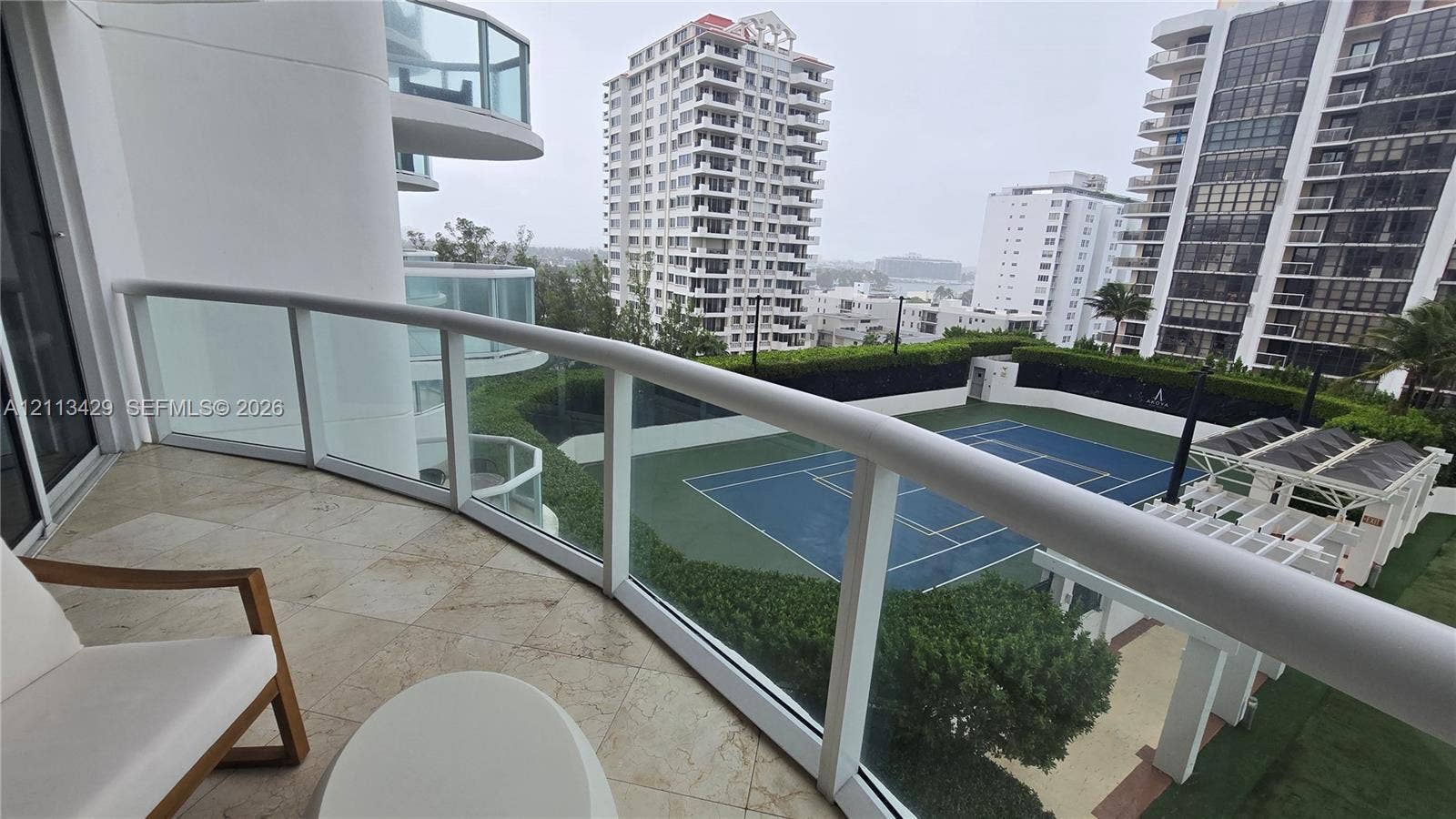 6365 Collins Avenue, #909, Miami Beach, FL 33141 Covered balcony featuring stone-tile flooring and a curved glass railing overlooking a tennis court