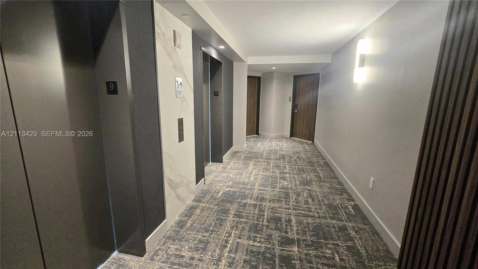 6365 Collins Avenue, #909, Miami Beach, FL 33141 Hallway featuring patterned wall-to-wall carpeting, stone-look elevator surround, recessed lighting, and wall-mounted sconces