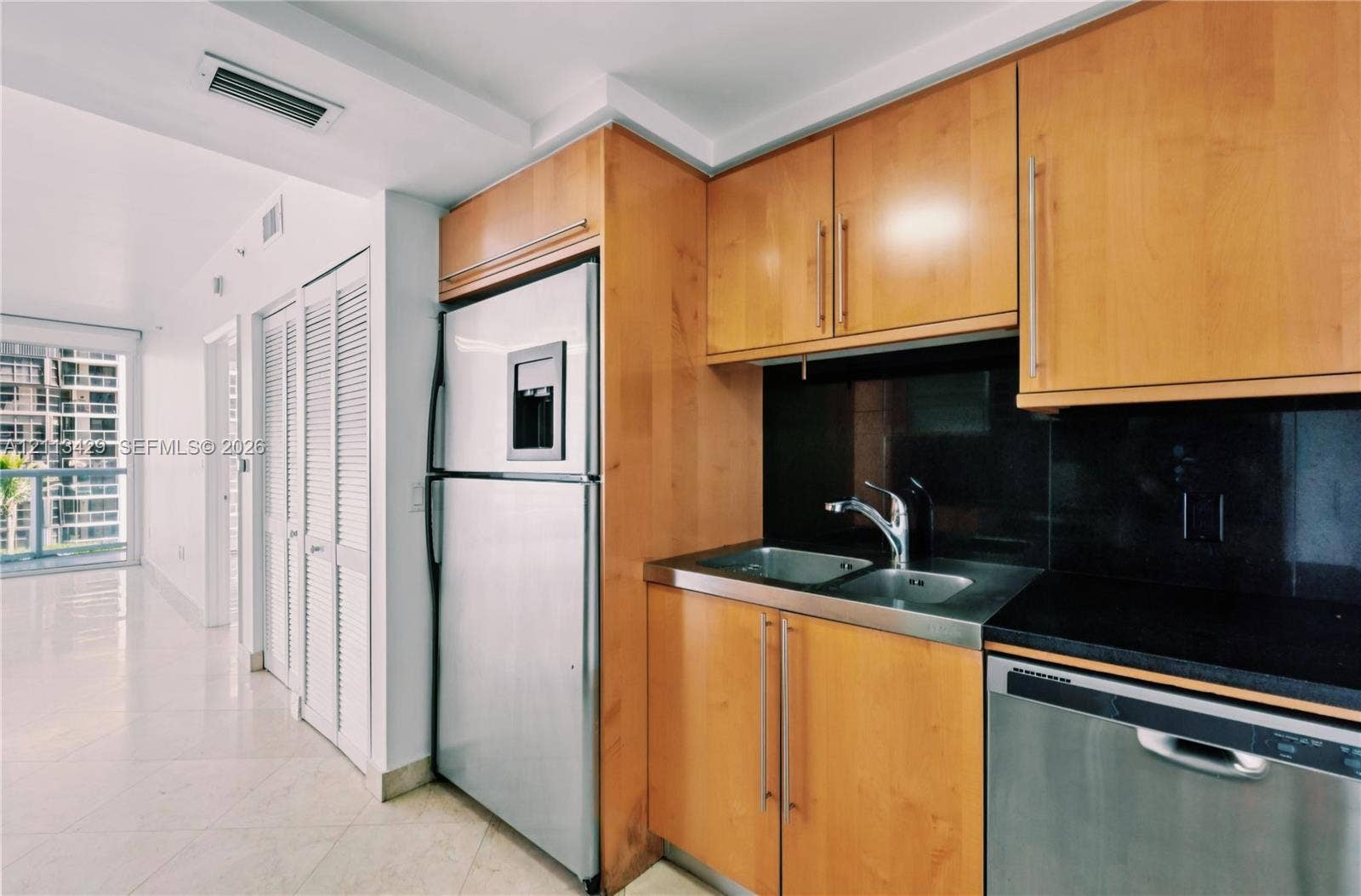 6365 Collins Avenue, #909, Miami Beach, FL 33141 Kitchen featuring flat-panel wood cabinetry, black solid-surface countertops, dual-basin stainless steel sink with high-arc faucet, and stainless steel appliances