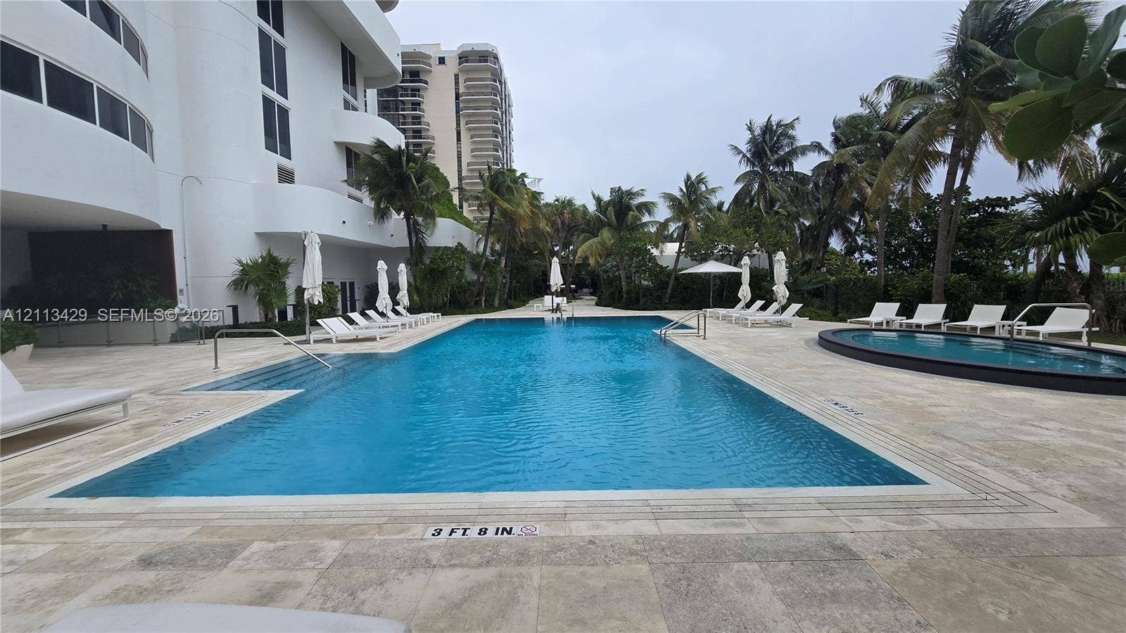 6365 Collins Avenue, #909, Miami Beach, FL 33141 Rectangular swimming pool with stone-tiled decking and an attached circular spa surrounded by mature palm trees