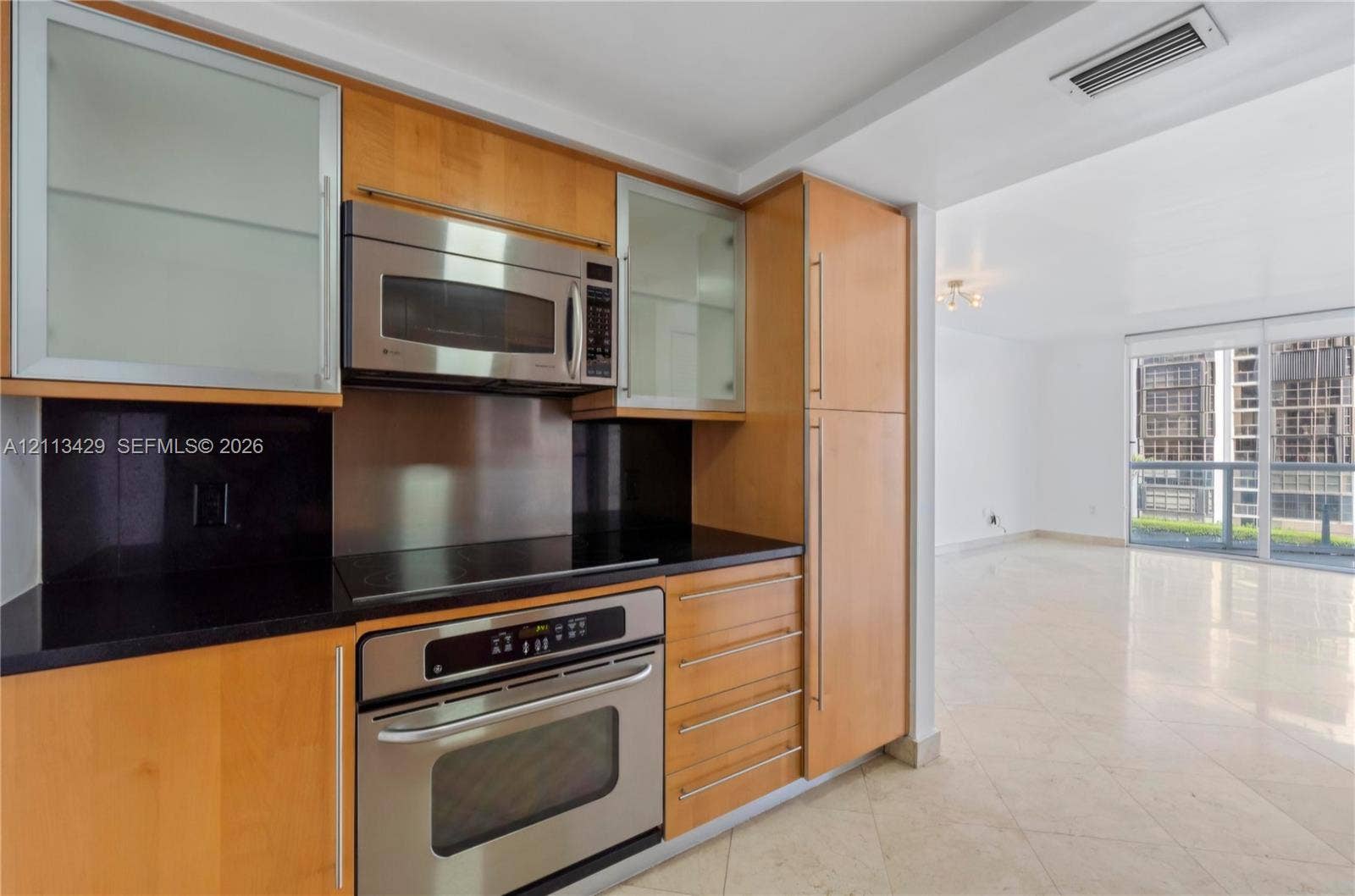 6365 Collins Avenue, #909, Miami Beach, FL 33141 Kitchen featuring flat-panel wood cabinetry, black countertops, stainless steel appliances, and glass-front upper cabinet doors