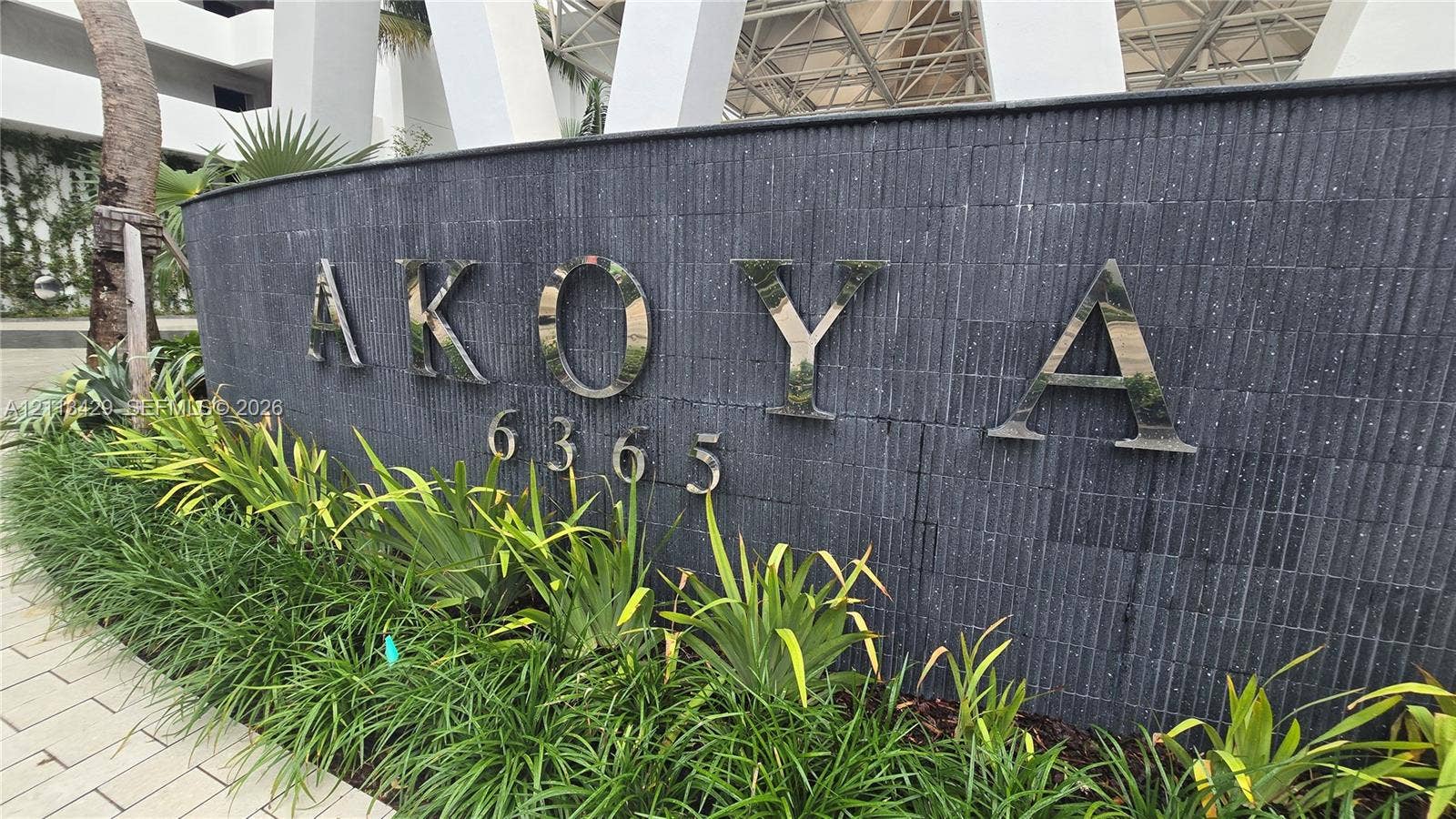 6365 Collins Avenue, #909, Miami Beach, FL 33141 Curved wall finished in stacked charcoal stone featuring polished metal dimensional lettering, numeric address signage, and a manicured foundation landscape