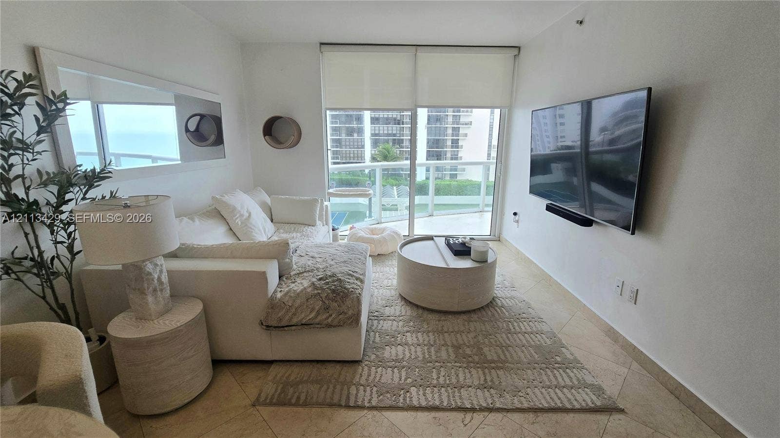 6365 Collins Avenue, #909, Miami Beach, FL 33141 Living space featuring stone-finish tile flooring, wall-mounted television, floor-to-ceiling sliding glass doors, and a private balcony with glass railing