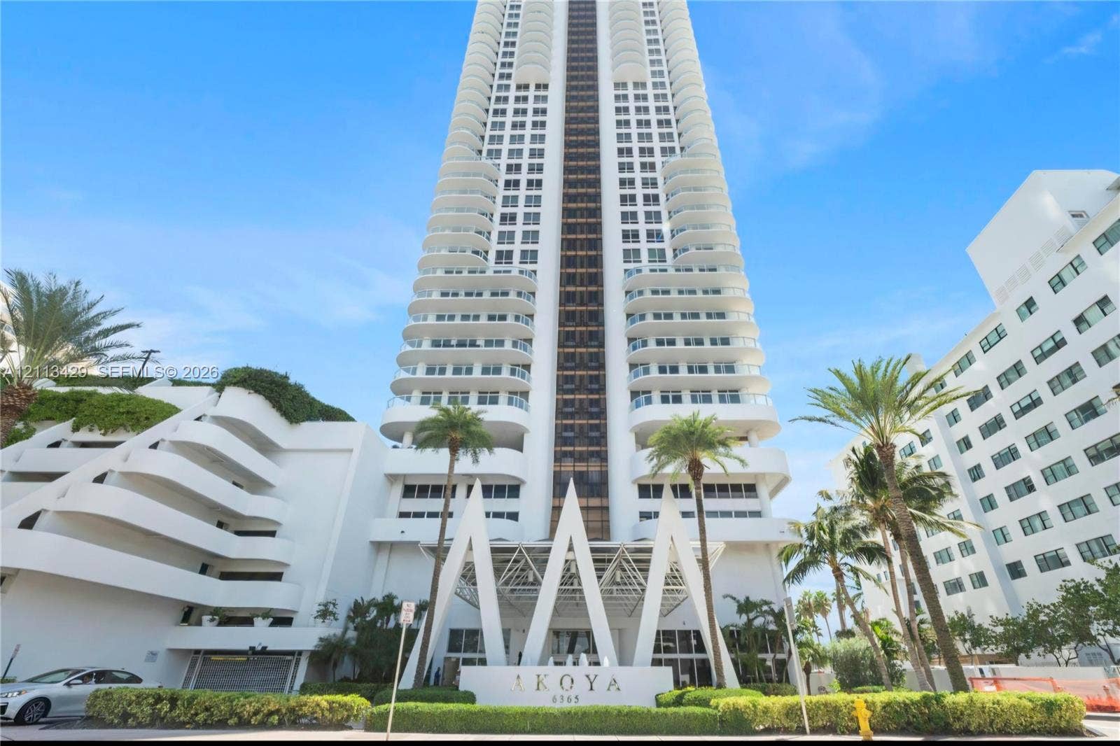 6365 Collins Avenue, #909, Miami Beach, FL 33141 High-rise residential tower featuring a white facade, structural balconies, geometric entryway architecture, and established landscaping