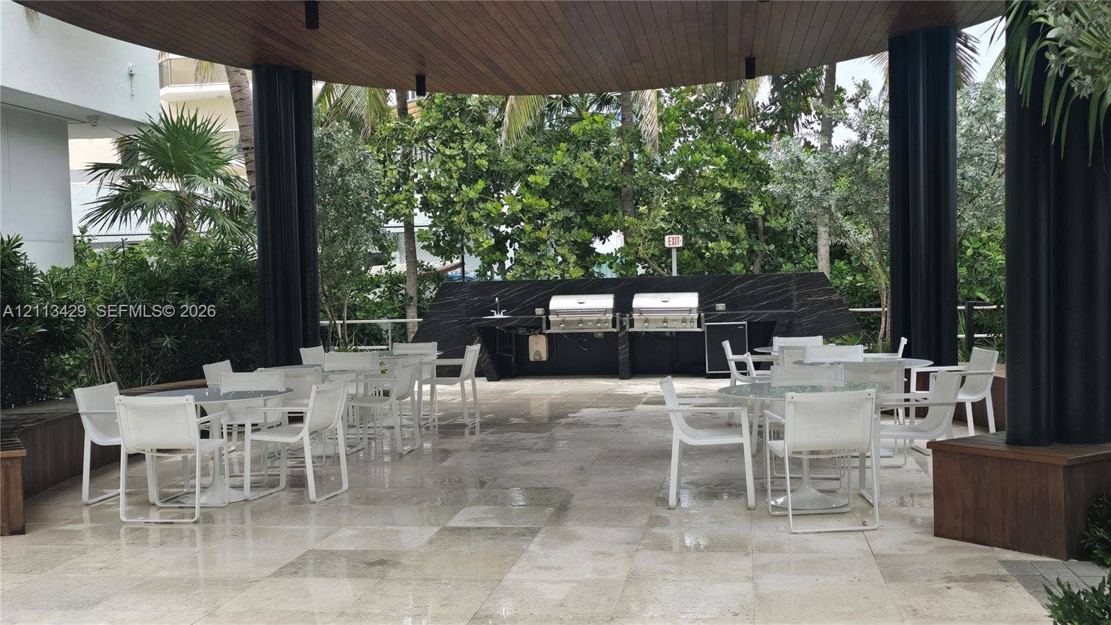 6365 Collins Avenue, #909, Miami Beach, FL 33141 Covered outdoor kitchen featuring stone flooring, a dark stone backsplash, dual stainless steel grills, and a wood-paneled ceiling