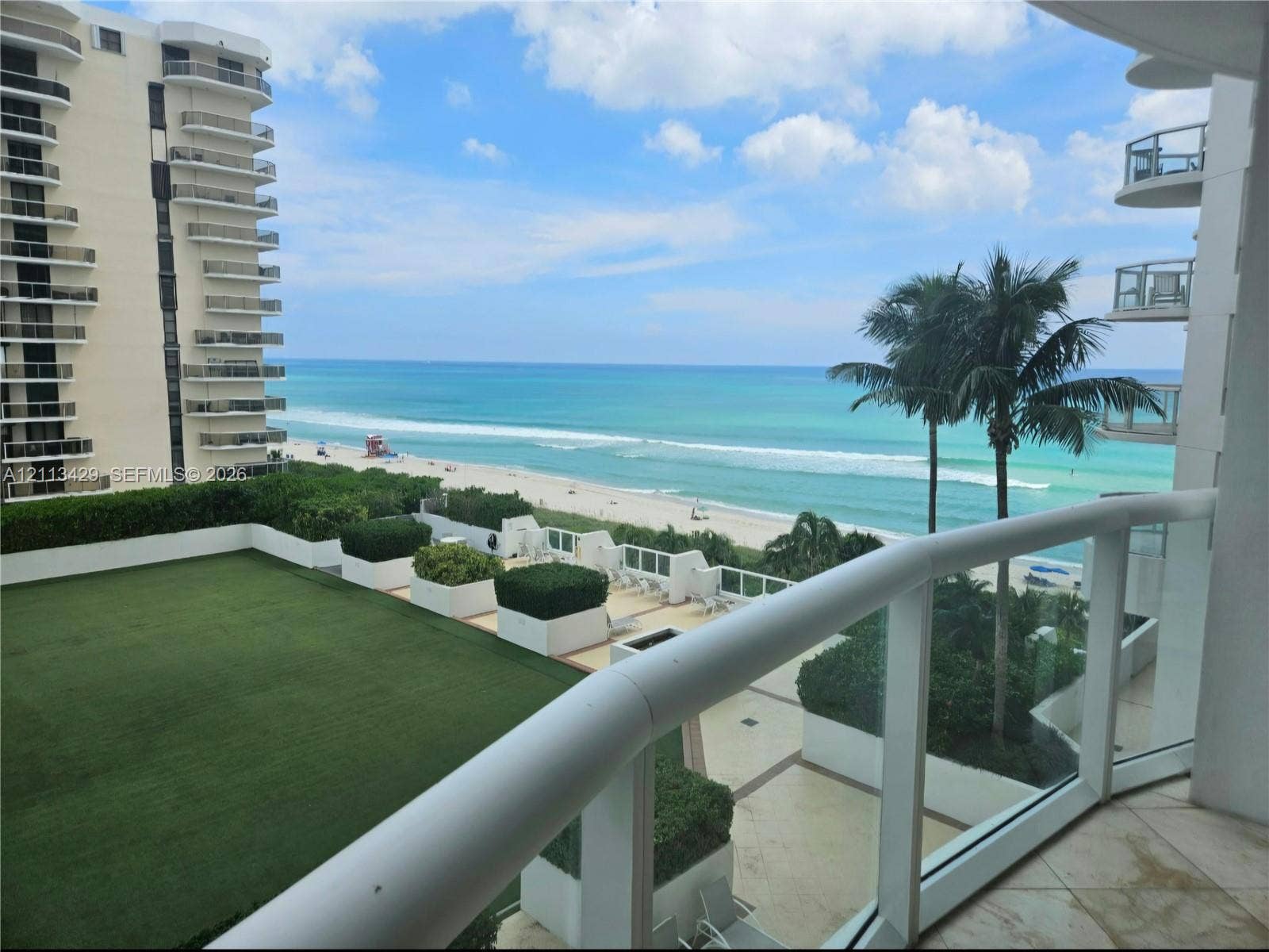 6365 Collins Avenue, #909, Miami Beach, FL 33141 Private balcony featuring a glass panel railing, stone tile flooring, an expansive synthetic turf terrace, built-in planter boxes with integrated landscaping, and oceanfront exposure
