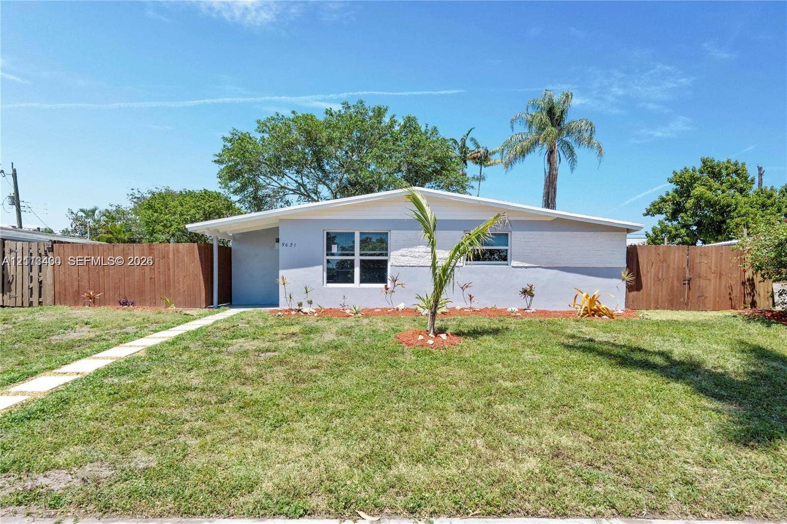 5621 SW 38th Court, Davie, Davie, FL 33314 Single-story residence featuring a painted masonry exterior, low-pitch roofline, horizontal wood fencing, and a concrete paver walkway