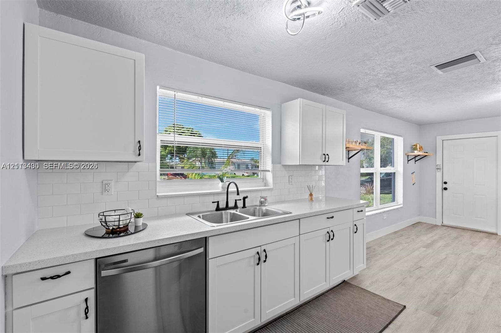5621 SW 38th Court, Davie, Davie, FL 33314 Kitchen featuring white shaker-style cabinetry, white subway tile backsplash, solid-surface countertops, dual-basin stainless steel sink with matte black hardware, and wood-finish flooring