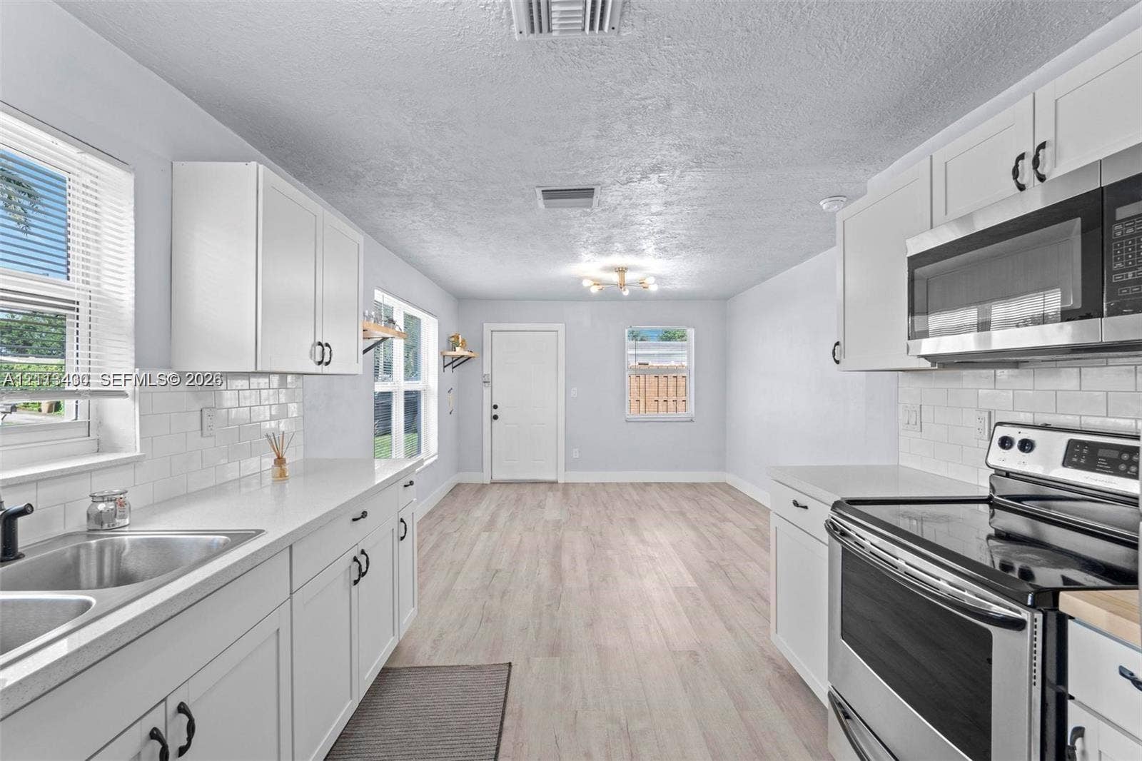 5621 SW 38th Court, Davie, Davie, FL 33314 Kitchen featuring white shaker-style cabinetry, white subway tile backsplash, solid-surface countertops, stainless steel appliances, and wood-finish flooring