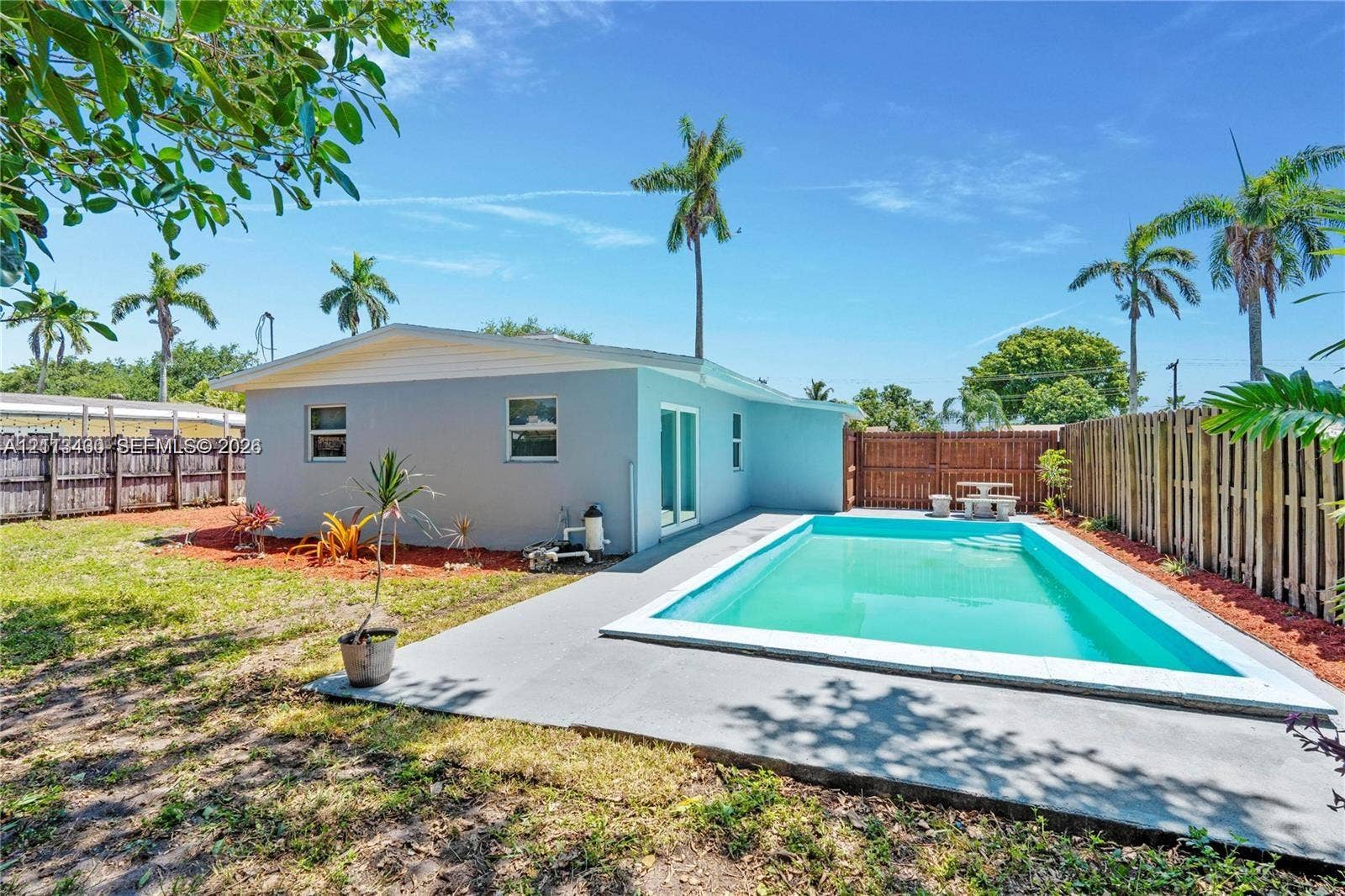 5621 SW 38th Court, Davie, Davie, FL 33314 Rear exterior featuring a rectangular inground swimming pool, concrete pool deck, wood-style privacy fencing, and exterior landscape beds