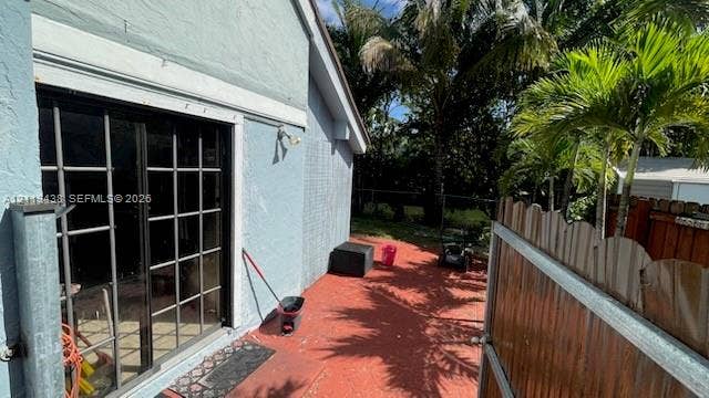 Exterior patio featuring a painted concrete floor, sliding glass doors with grid detailing, and a wooden privacy fence