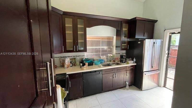 Kitchen featuring dark wood cabinetry, light-toned countertops, tile flooring, glass-paneled upper cabinets, and stainless steel appliances