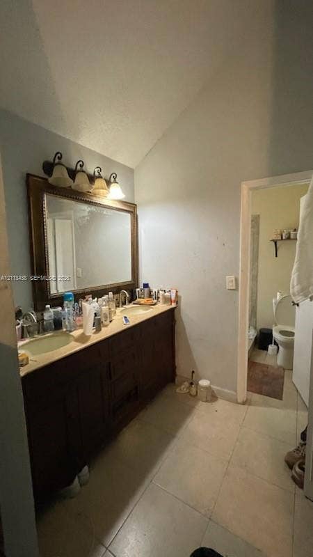 Dual-sink vanity with a stone countertop, stained wood cabinetry, a large framed mirror, and a multi-light fixture with glass shades