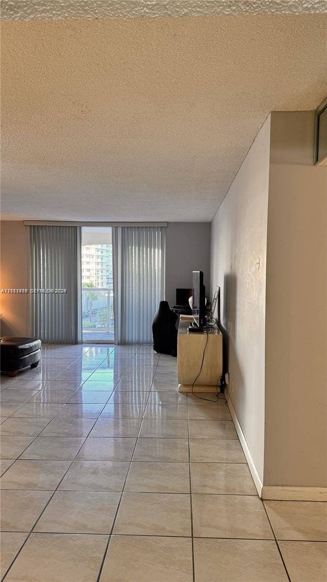 3800 S Ocean Drive, #416, Hollywood, FL 33019 Open interior space featuring light-toned tile flooring and full-height vertical blinds leading to an exterior balcony