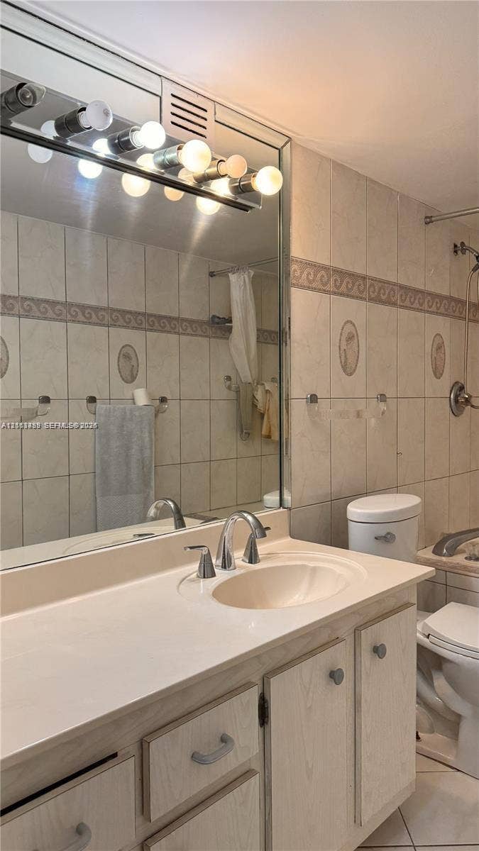 3800 S Ocean Drive, #416, Hollywood, FL 33019 Bathroom featuring a vanity with integrated sink, expansive wall-to-wall mirror, multi-bulb overhead lighting, and full-height tiled walls with decorative trim