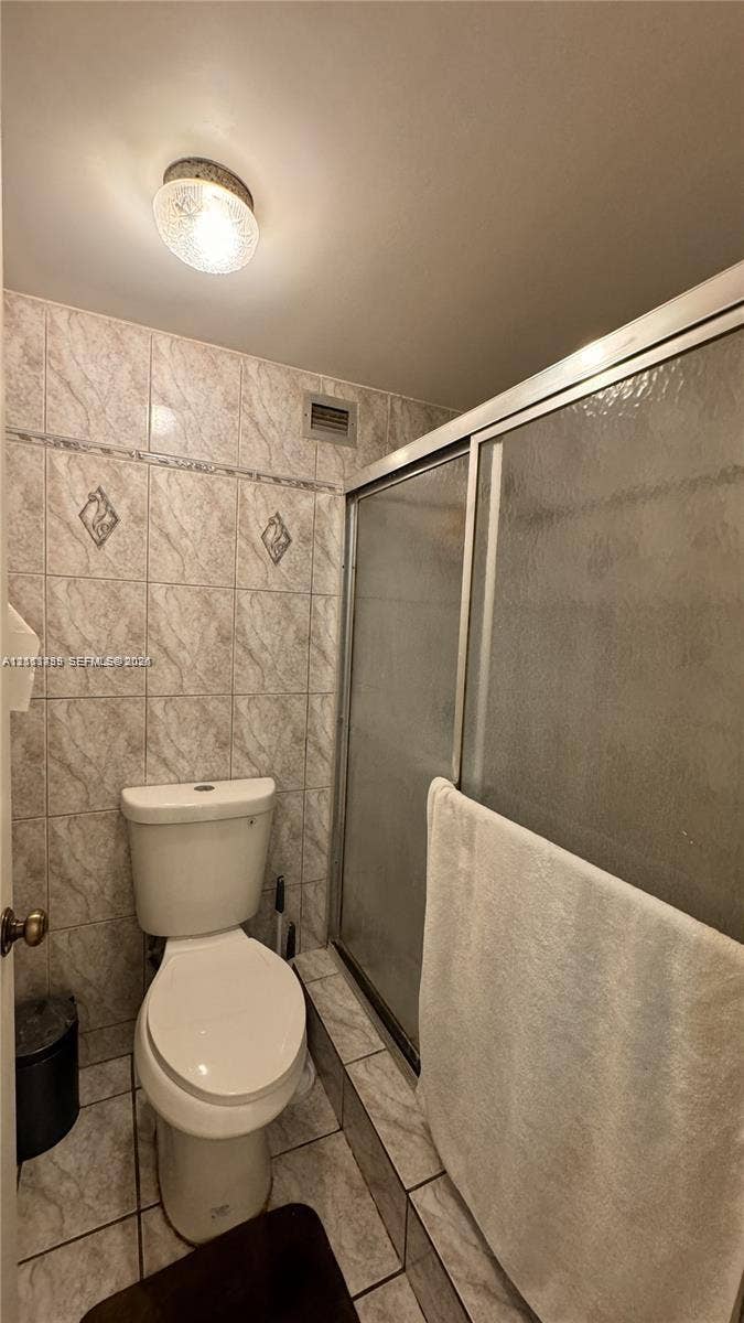 3800 S Ocean Drive, #416, Hollywood, FL 33019 Full-height tiled walls featuring decorative diamond-patterned inserts, walk-in shower with a glass door, ceramic tile flooring, and a flush-mount ceiling light fixture