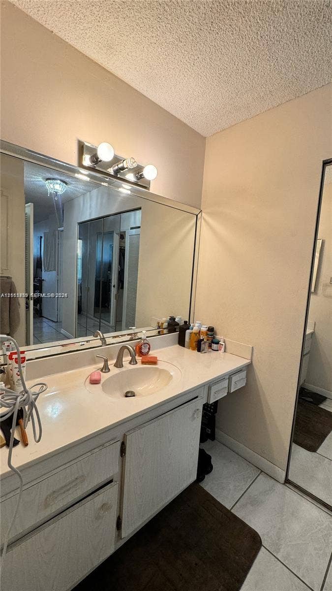 3800 S Ocean Drive, #416, Hollywood, FL 33019 Vanity featuring a light-toned wood-finish cabinet, integrated countertop with a circular basin, chrome-finish faucet, full-width wall-mounted mirror, and three-bulb vanity light fixture