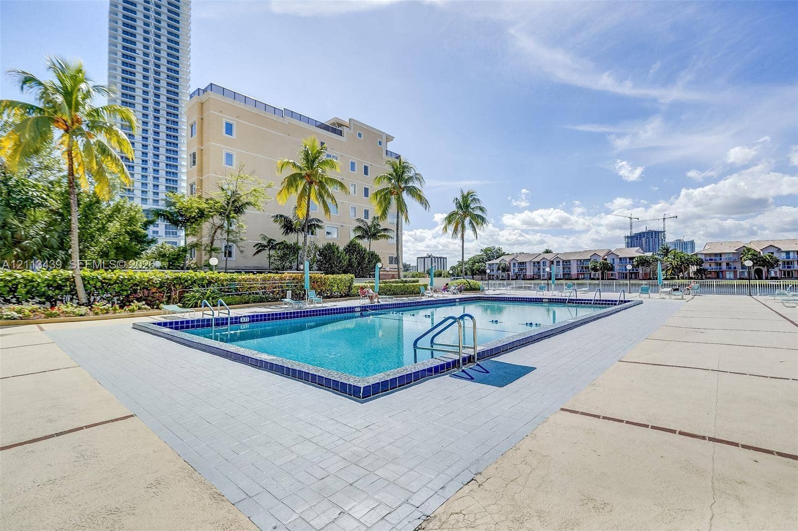 3800 S Ocean Drive, #416, Hollywood, FL 33019 Swimming pool featuring tile trim, metal handrails, and a surrounding paved deck with mature palm trees
