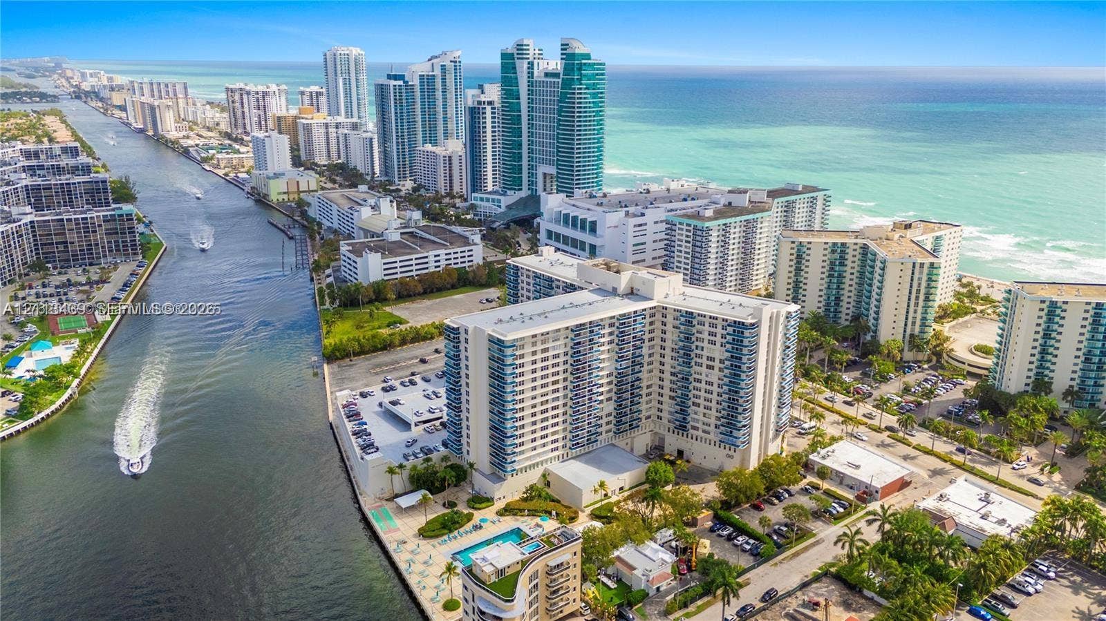 3800 S Ocean Drive, #416, Hollywood, FL 33019 Aerial perspective of a multi-story residential complex situated at the intersection of a coastal waterway and the ocean, featuring waterfront access, paved surface parking, a swimming pool, and landscaping