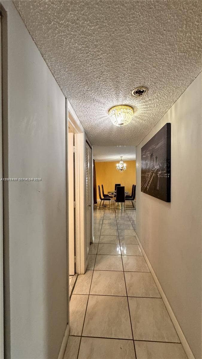 3800 S Ocean Drive, #416, Hollywood, FL 33019 Hallway featuring large-format ceramic tile flooring, textured ceiling, flush-mount decorative lighting, and louvered closet doors
