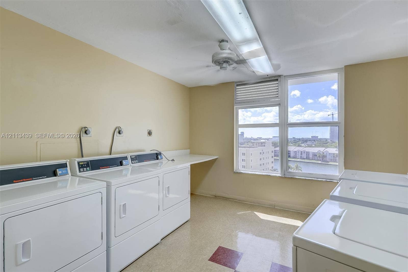 3800 S Ocean Drive, #416, Hollywood, FL 33019 Utility room featuring multiple high-capacity washer and dryer units, expansive built-in workspace counter, large window with natural light, and ceiling-mounted lighting