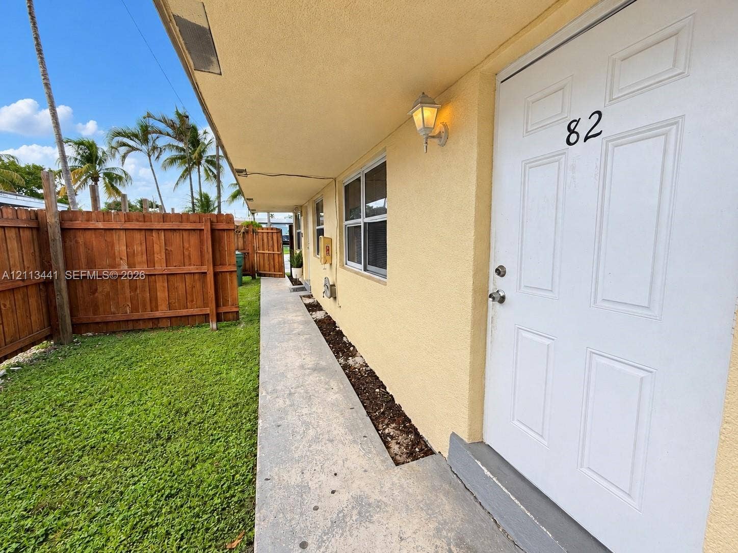 80 NE 36th Court, #82, Oakland Park, Oakland Park, FL 33334 Exterior walkway with concrete paving, wood privacy fencing, and an attached outdoor sconce