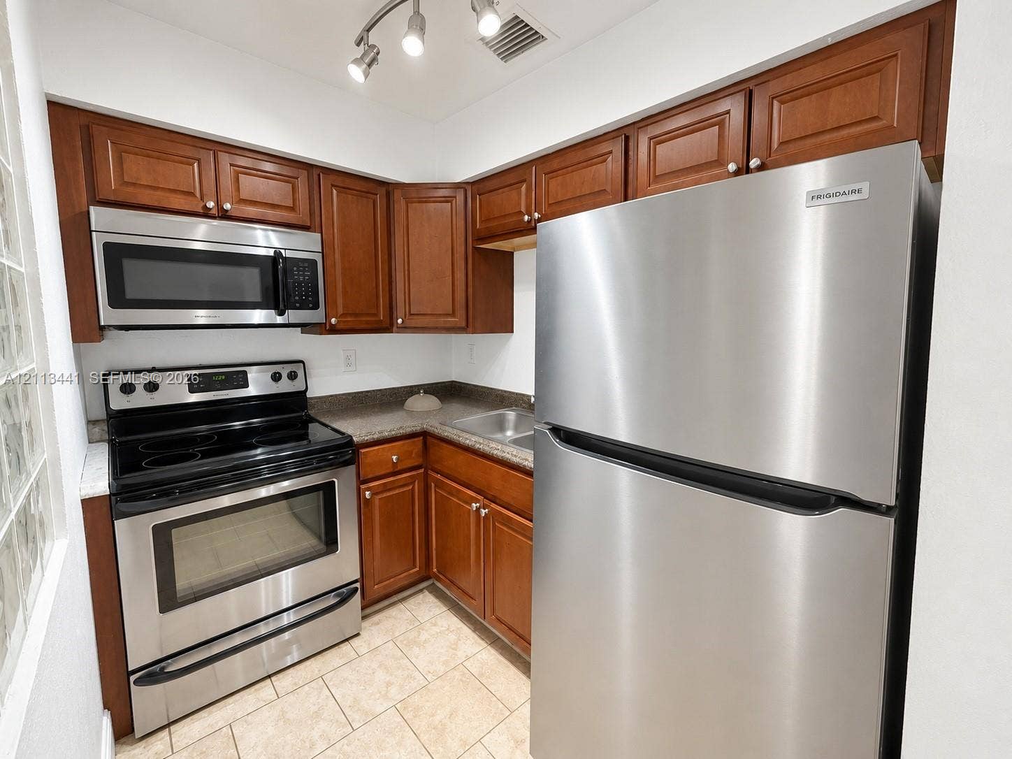 80 NE 36th Court, #82, Oakland Park, Oakland Park, FL 33334 Kitchen featuring stainless steel appliances, wood cabinetry, stone-finish countertops, ceramic tile flooring, and adjustable track lighting