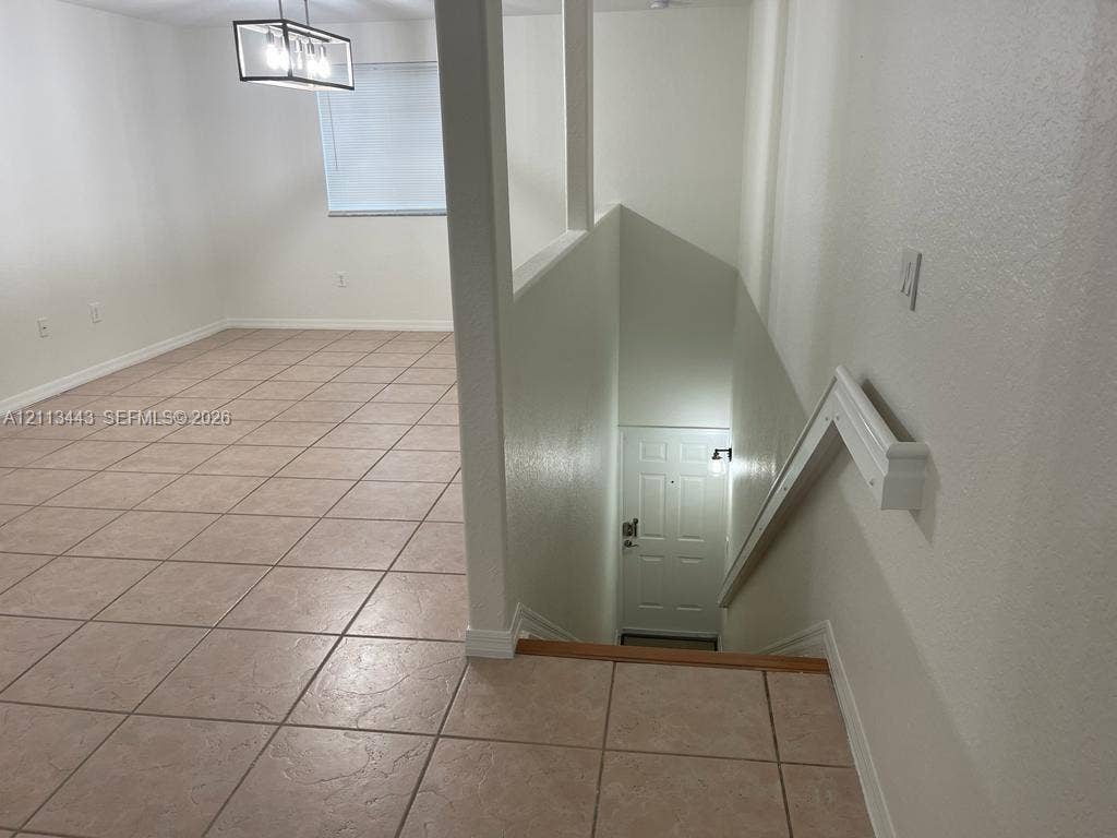 5705 NW 109th Avenue, #47, Doral, Doral, FL 33178 Ceramic tile flooring throughout the open interior space, featuring a modern rectangular pendant light fixture and a stairway with white wood handrails leading to an exterior entrance door