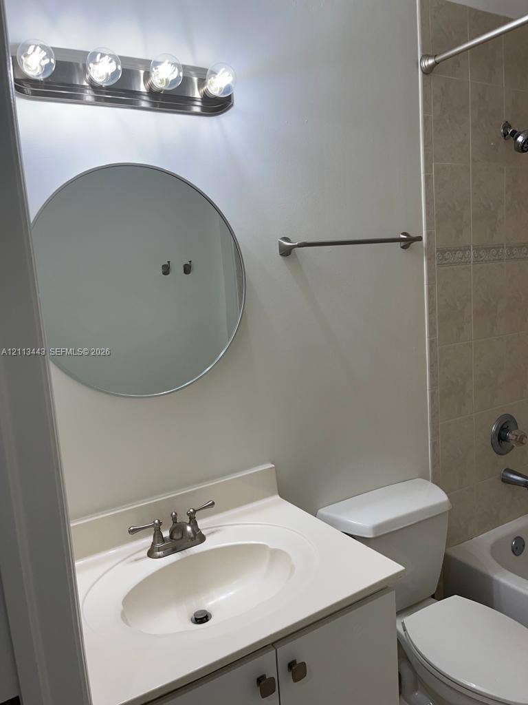 5705 NW 109th Avenue, #47, Doral, Doral, FL 33178 Bathroom featuring a round mirror, four-bulb vanity light fixture, vanity with an integrated sink, and a tiled shower surround