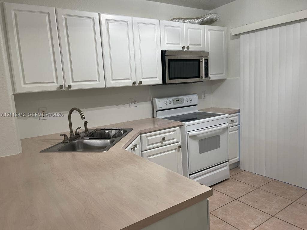 5705 NW 109th Avenue, #47, Doral, Doral, FL 33178 Kitchen featuring white shaker-style cabinetry, a stainless steel over-the-range microwave, a neutral-toned countertop, a double-basin stainless steel sink with a high-arch faucet, and ceramic tile flooring