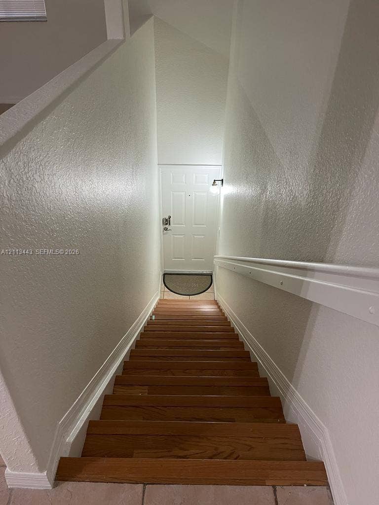 5705 NW 109th Avenue, #47, Doral, Doral, FL 33178 Staircase featuring wood-finish treads, a white wall-mounted handrail, and high-contrast paint finishes, leading to a panel-style entry door