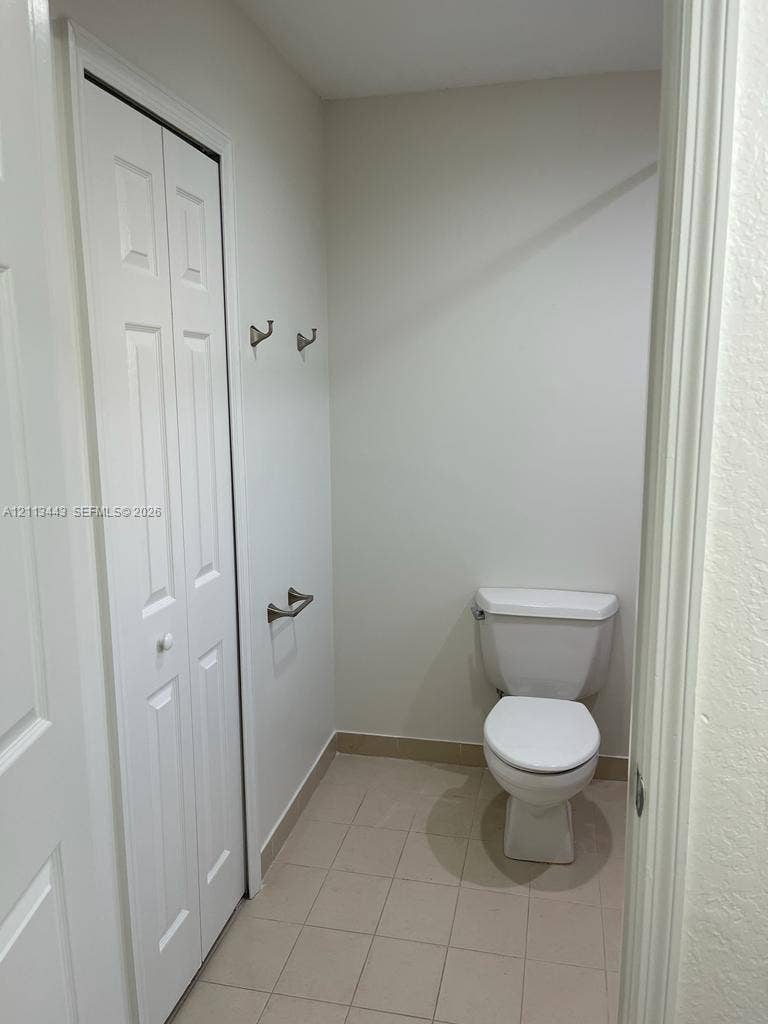 5705 NW 109th Avenue, #47, Doral, Doral, FL 33178 Neutral-toned interior space featuring light-colored tile flooring, white bi-fold closet doors, a porcelain toilet, and wall-mounted brushed nickel hardware