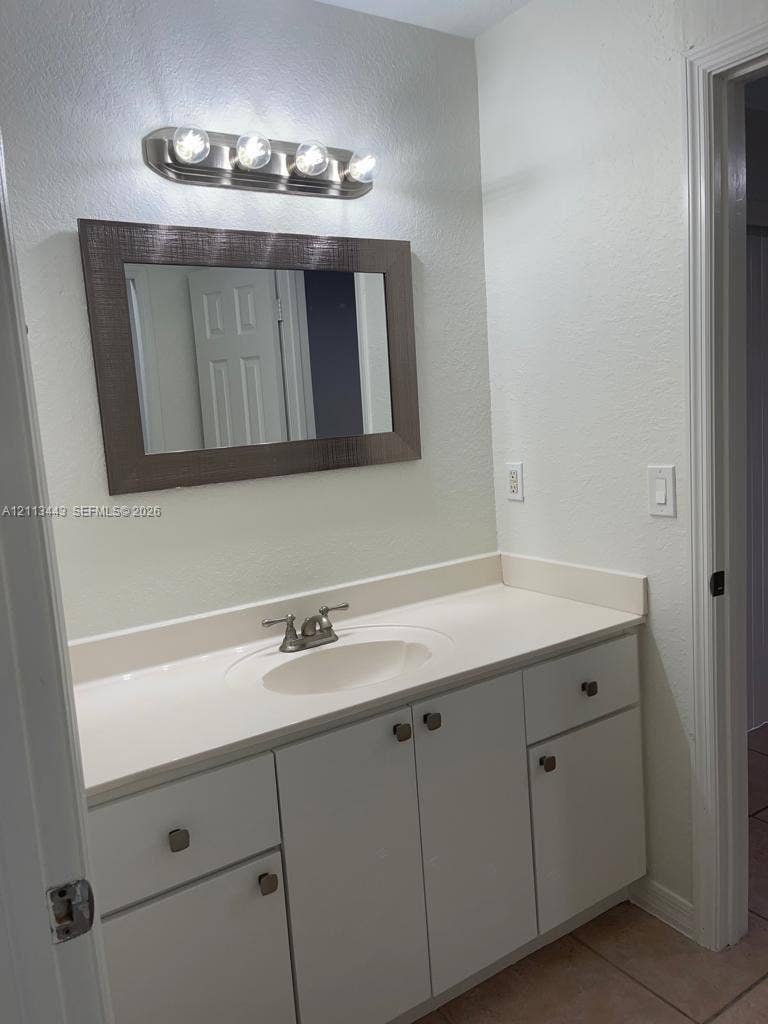 5705 NW 109th Avenue, #47, Doral, Doral, FL 33178 Bathroom vanity featuring white cabinetry, a solid-surface countertop with an integrated oval sink, chrome dual-handle faucet, framed wall mirror, and a four-bulb vanity light fixture