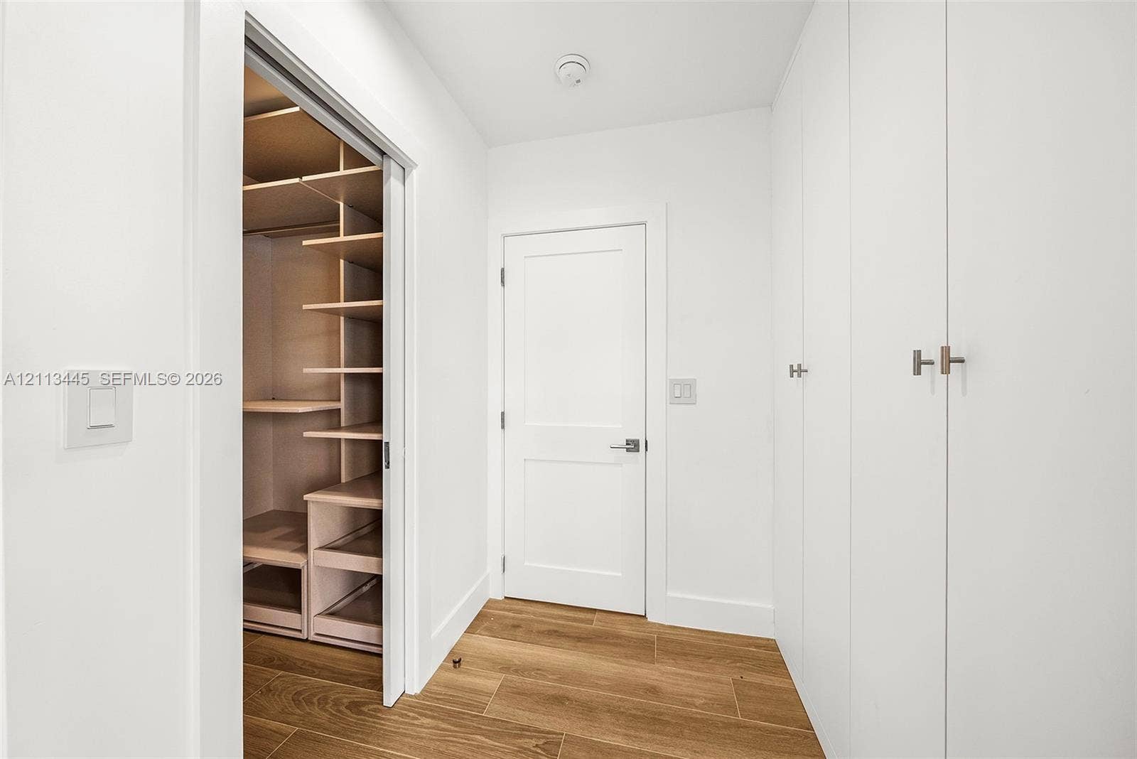 6951 SW 134th Street, Pinecrest, Pinecrest, FL 33156 Walk-in closet featuring custom shelving and pull-out drawers, complemented by floor-to-ceiling built-in cabinetry, white shaker-style doors, and wood-finish flooring