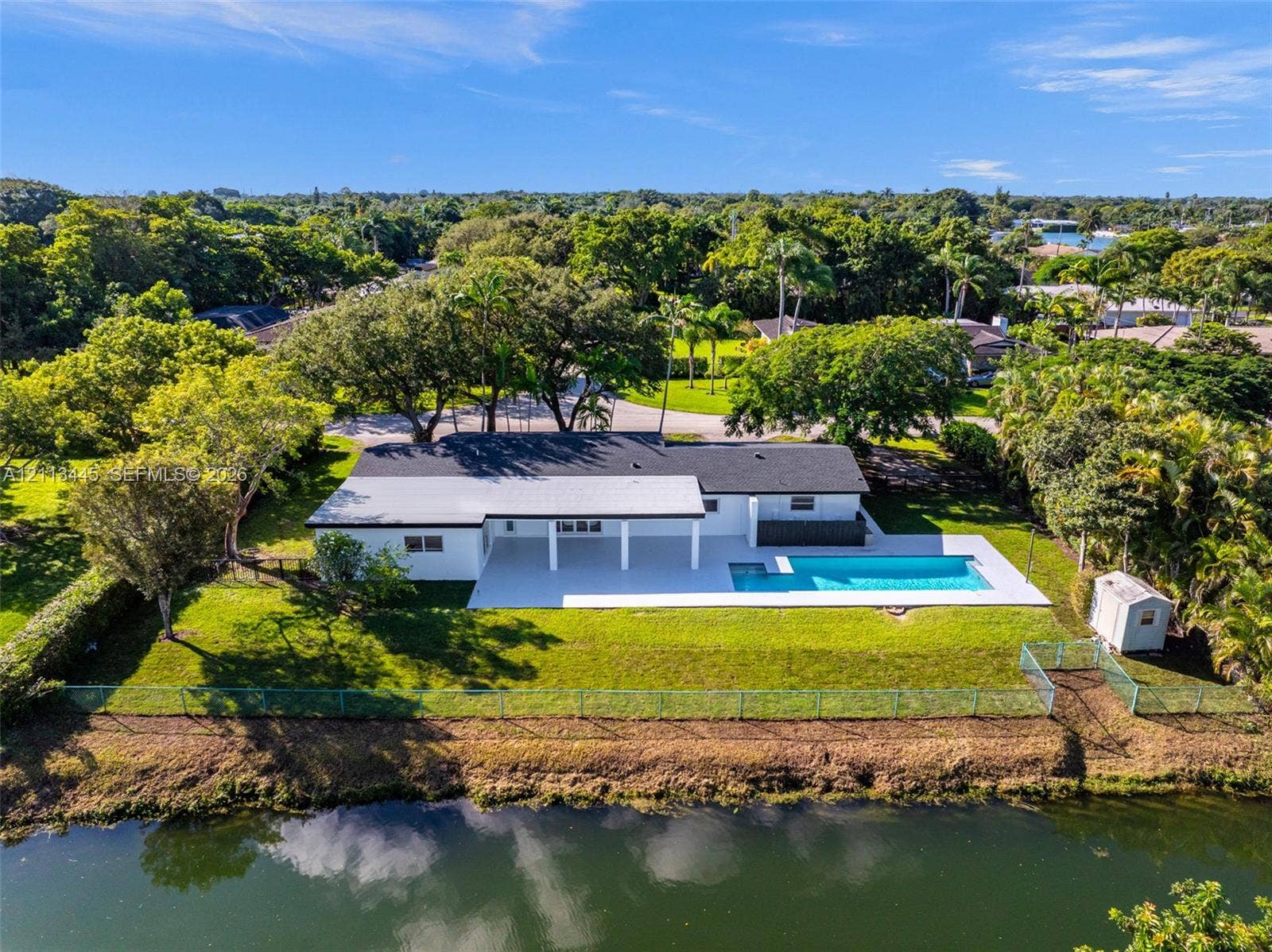 6951 SW 134th Street, Pinecrest, Pinecrest, FL 33156 Waterfront property featuring a swimming pool, covered patio, expansive lawn, and mature trees