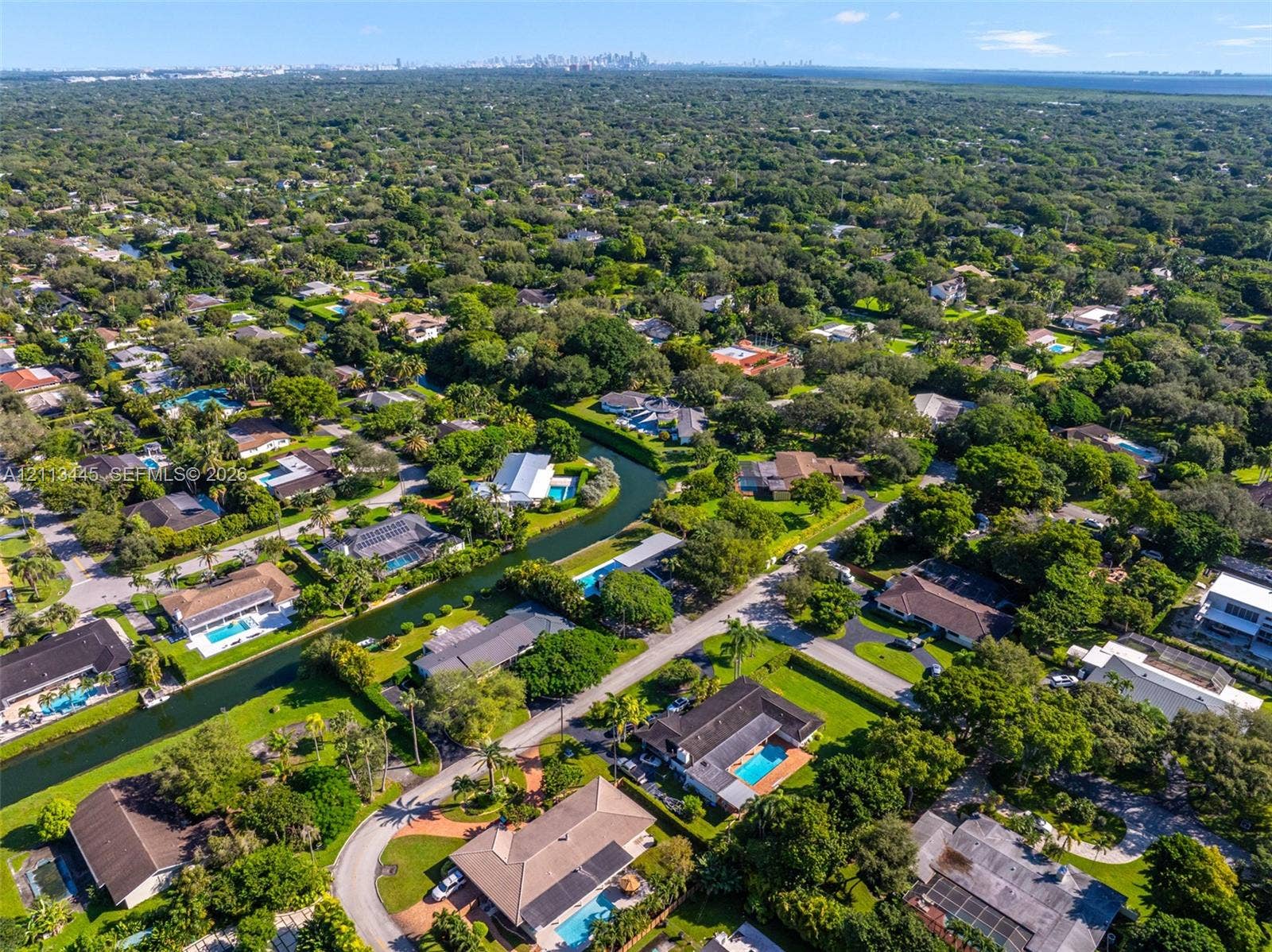 6951 SW 134th Street, Pinecrest, Pinecrest, FL 33156 Aerial perspective of a residential neighborhood featuring mature tree canopies, paved street infrastructure, and multiple properties with private swimming pools and water-front canal access