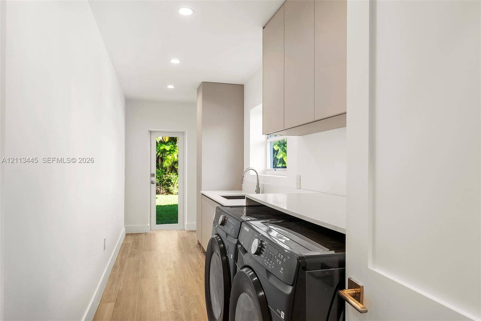 6951 SW 134th Street, Pinecrest, Pinecrest, FL 33156 Laundry area featuring minimalist flat-panel cabinetry, light-toned stone-finish countertops, an undermount sink with a gooseneck faucet, wood-finish flooring, and recessed ceiling lighting