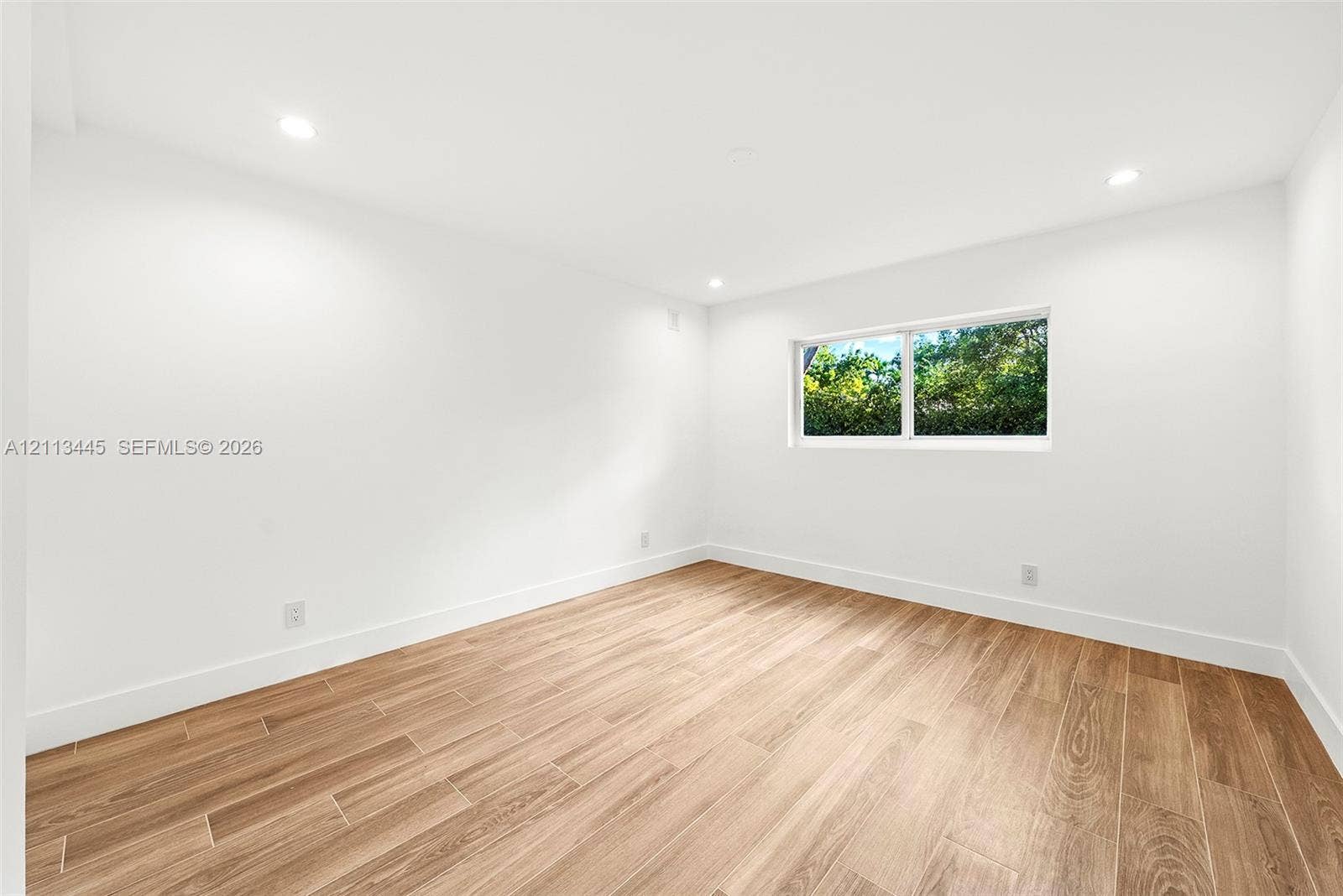 6951 SW 134th Street, Pinecrest, Pinecrest, FL 33156 Bright room featuring wood-finish flooring, crisp white wall finishes, recessed lighting, and a window with exterior greenery