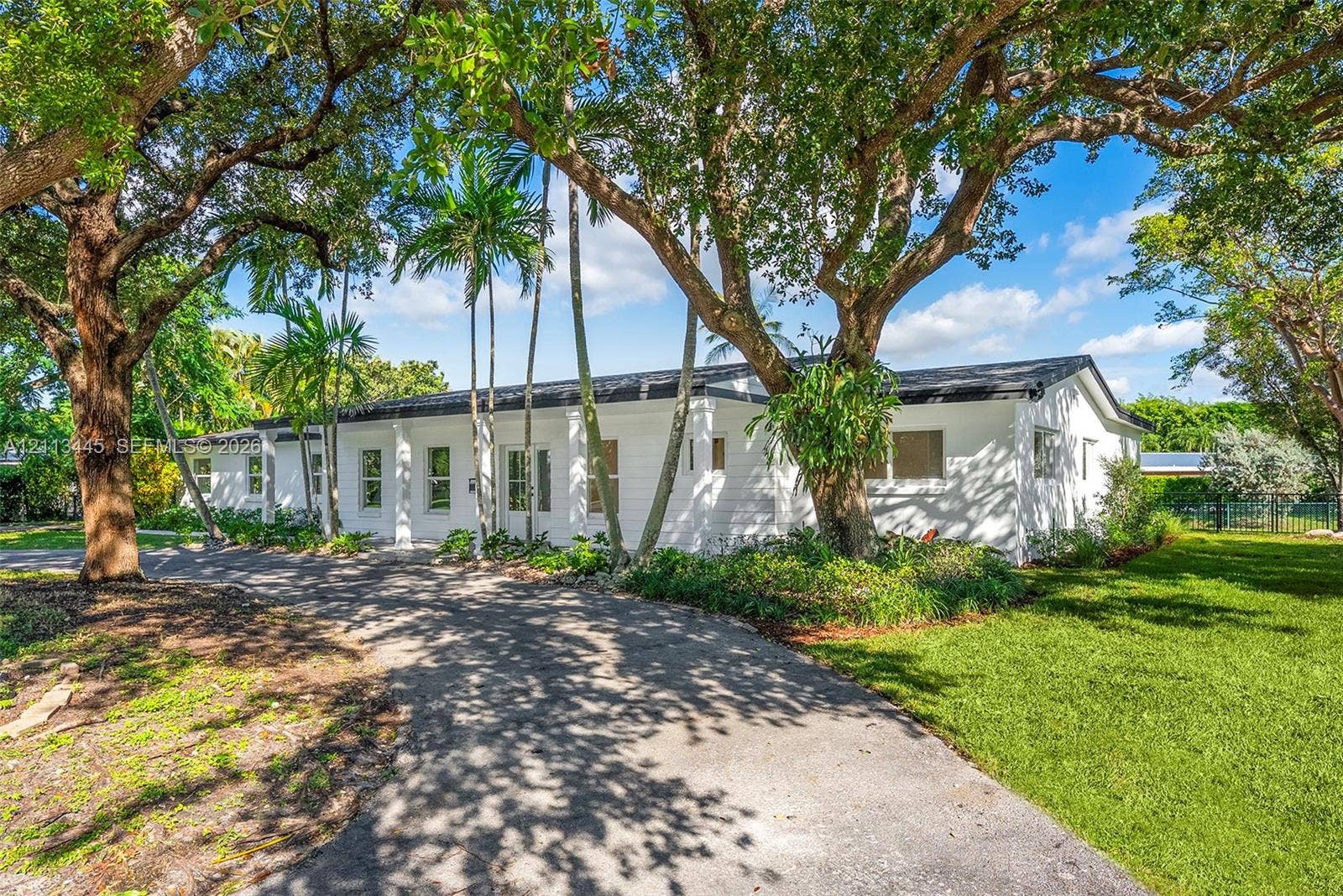 6951 SW 134th Street, Pinecrest, Pinecrest, FL 33156 Single-story residence featuring a white painted exterior, asphalt driveway, mature canopy trees, and established landscaping